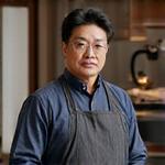 Tetsu no Ki代表取締役、清水様の肖像。作業着を着て、鍛造された鉄のオブジェの隣に立つ。真剣な眼差しから職人の情熱が伝わる。